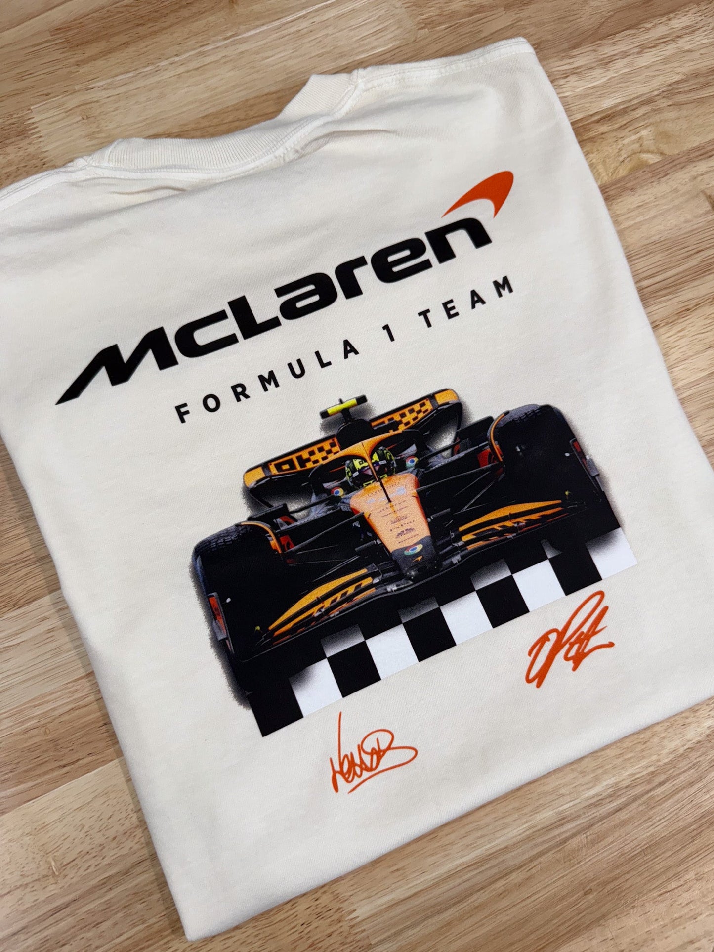 White t-shirt with McLaren Formula 1 Team logo and race car design on a wooden surface